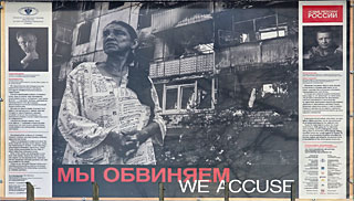 Een verdrietige vrouw staat bij een verwoest flatgebouw. De voorgeschiedenis ontbreekt. Mogelijk niet zonder reden.