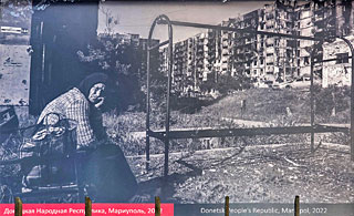 Een vrouw uit Marioepol zit bij de pakken neer bij iets wat een bushalte zou kunnen zijn geweest.